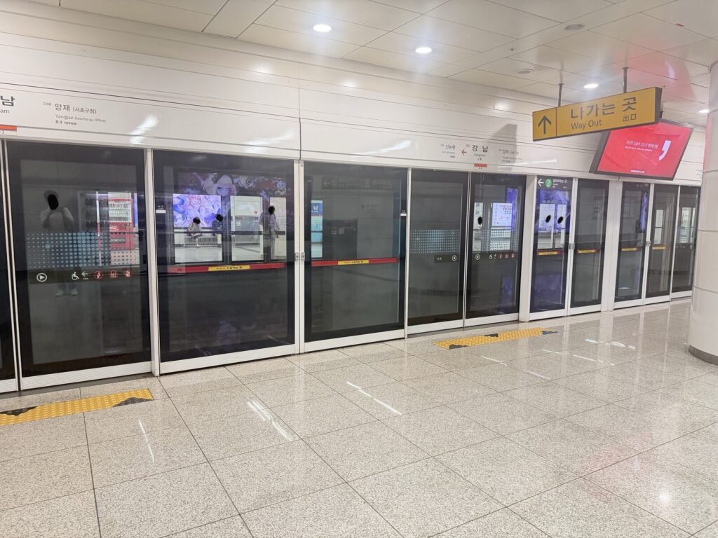 Platform screen doors and overhead signage at a subway station, with a transfer sign pointing toward Line 2