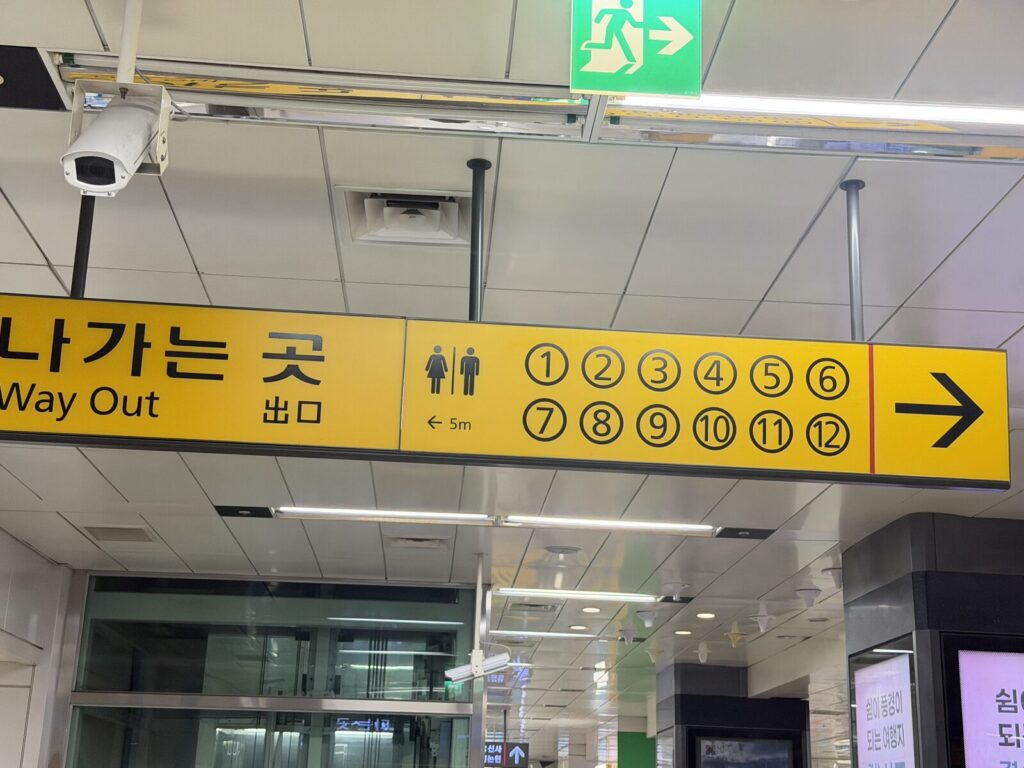 Overhead station sign showing numbered exits 1 through 12 and restroom direction