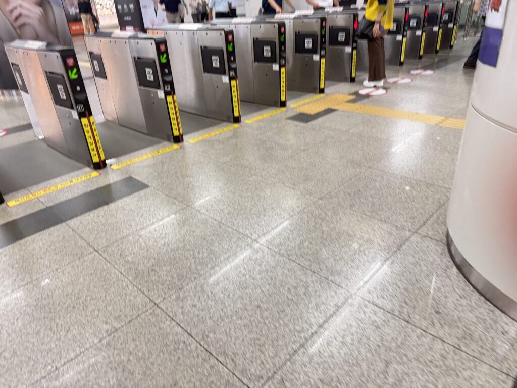 Row of subway turnstile gates with green arrow indicators and yellow tactile paving for accessibility