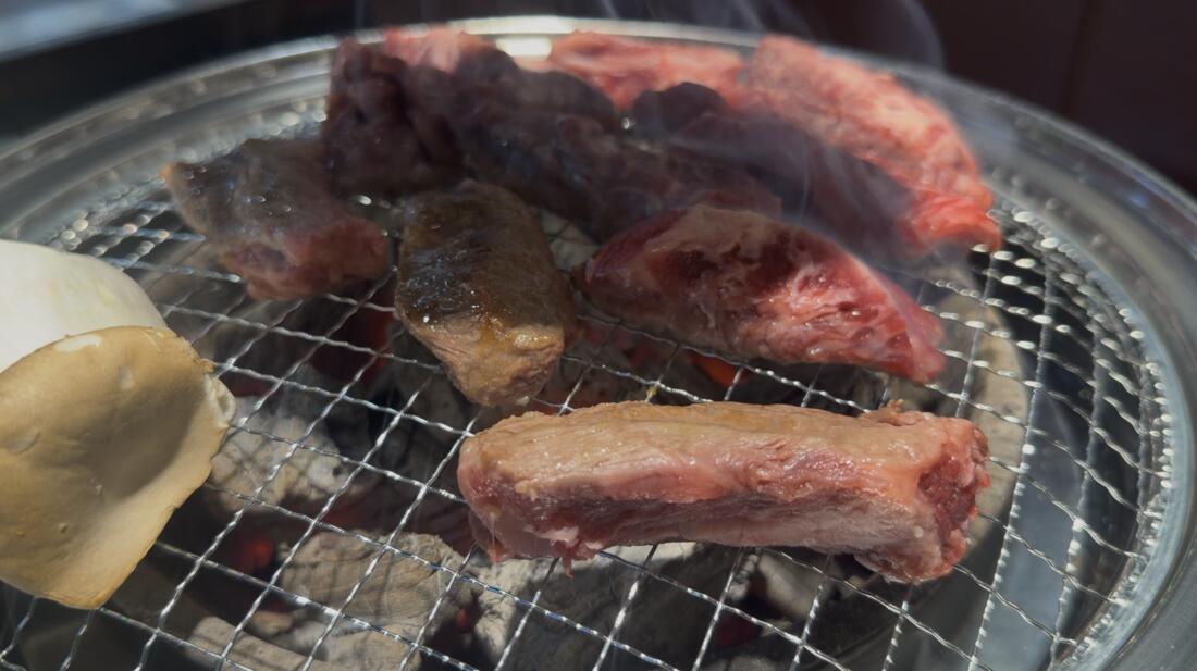 Korean beef short rib grilling on a charcoal grill with a king oyster mushroom at Umaju restaurant