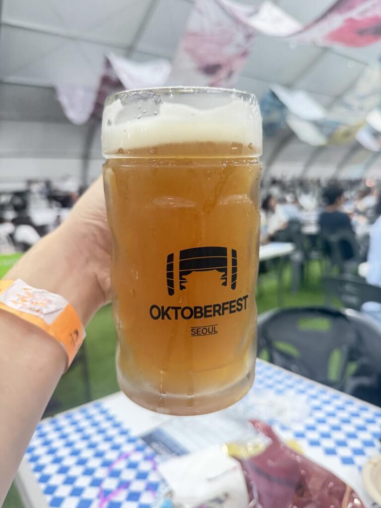 Hand holding an official Oktoberfest Seoul beer mug inside the festival tent