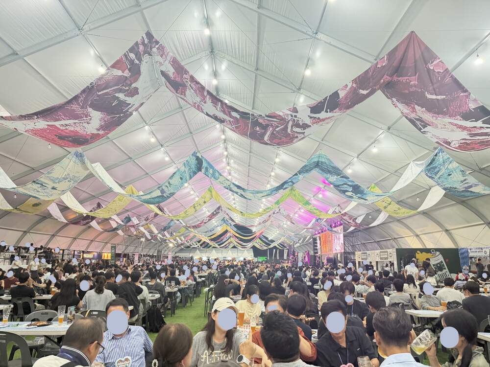Interior of the large Oktoberfest Seoul festival tent with colorful bunting overhead and a packed crowd at long tables